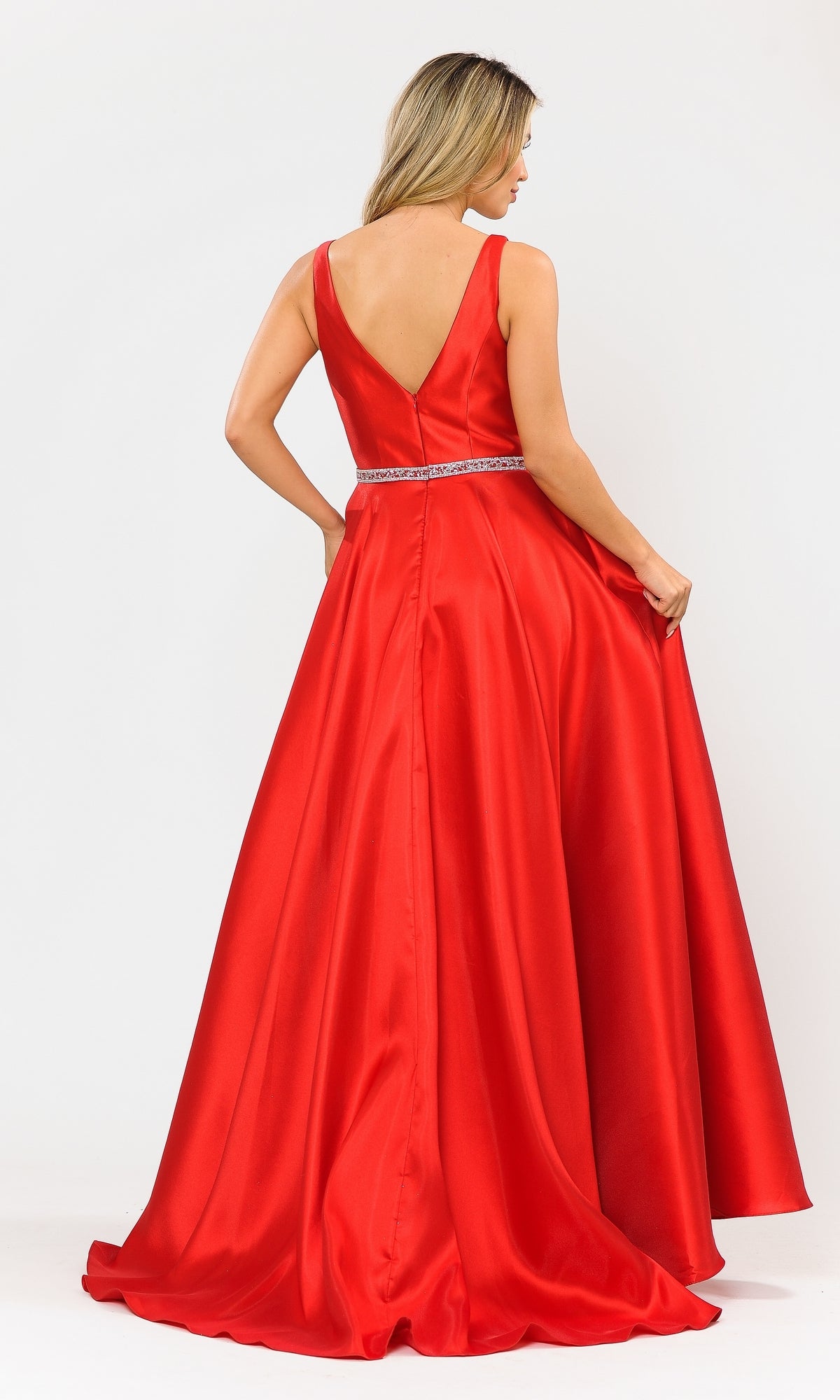 A woman stands holding the skirt of the Deep V-Neck Long Mikado A-Line Prom Dress 8682—a sleeveless, floor-length red gown with a V-back and beaded waistband.
